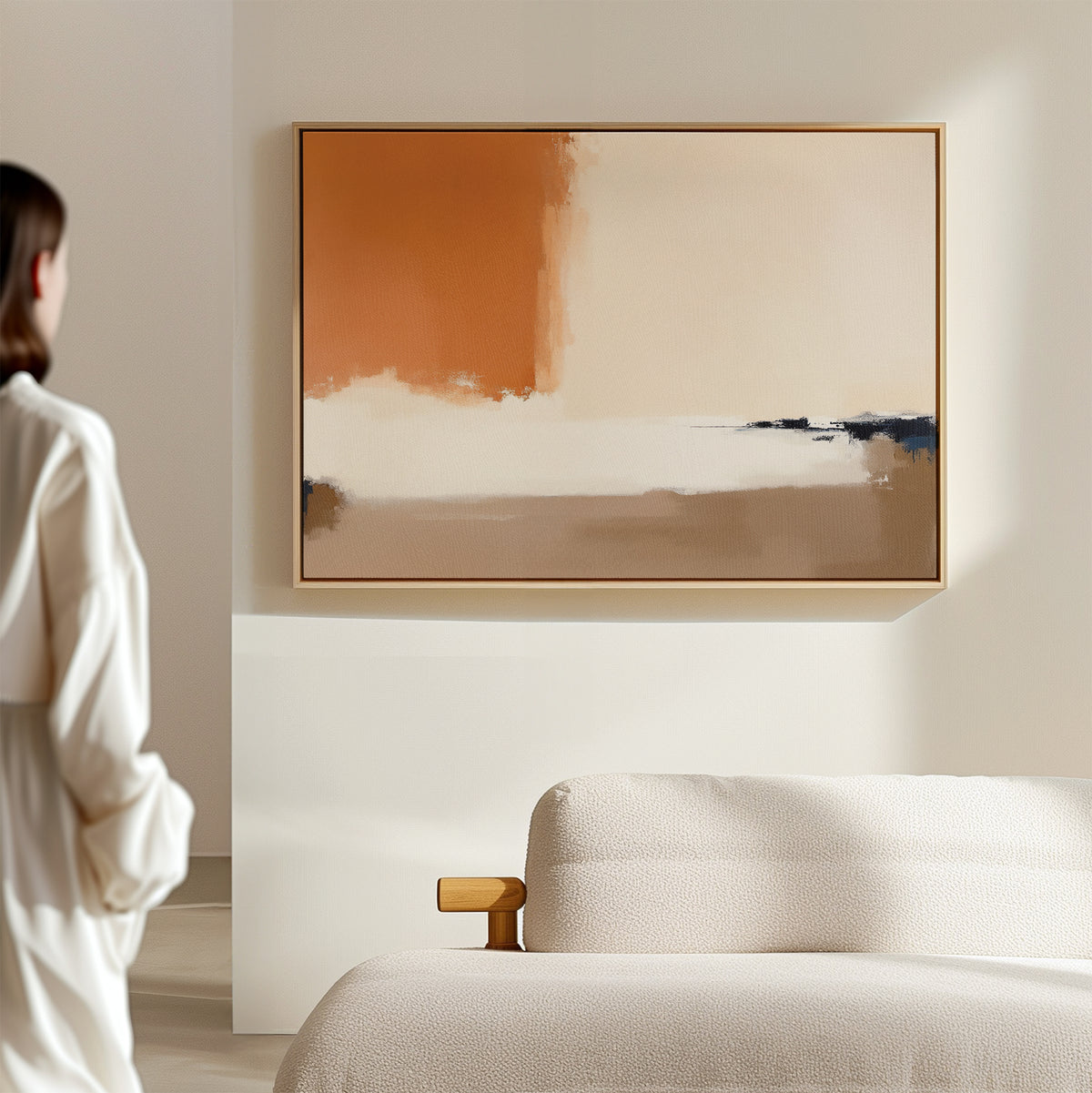 A person in a white shirt stands in a bright, minimalist room with a beige sofa, admiring the Terracotta Edge Canvas Art - Horizontal, which elevates the modern living room decor with its contemporary abstract earth tones.