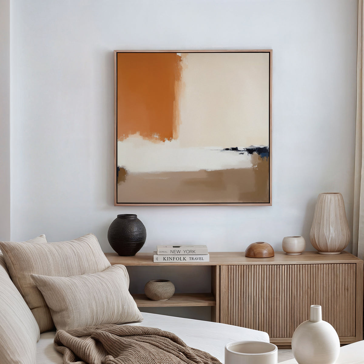 A modern living room with a beige sofa, neutral cushions, and a wooden sideboard adorned with vases and books. The Terracotta Edge Canvas Art - Square, in orange, cream, and beige hues, is displayed above on the white wall.