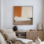 A modern living room with a beige sofa, neutral cushions, and a wooden sideboard adorned with vases and books. The Terracotta Edge Canvas Art - Square, in orange, cream, and beige hues, is displayed above on the white wall.