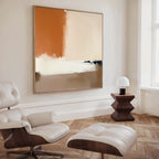 A modern living room features a white leather lounge chair and ottoman, geometric wood side table, and small white lamp by a large window, accented with the Terracotta Edge Canvas Art - Square for striking minimalist decor.