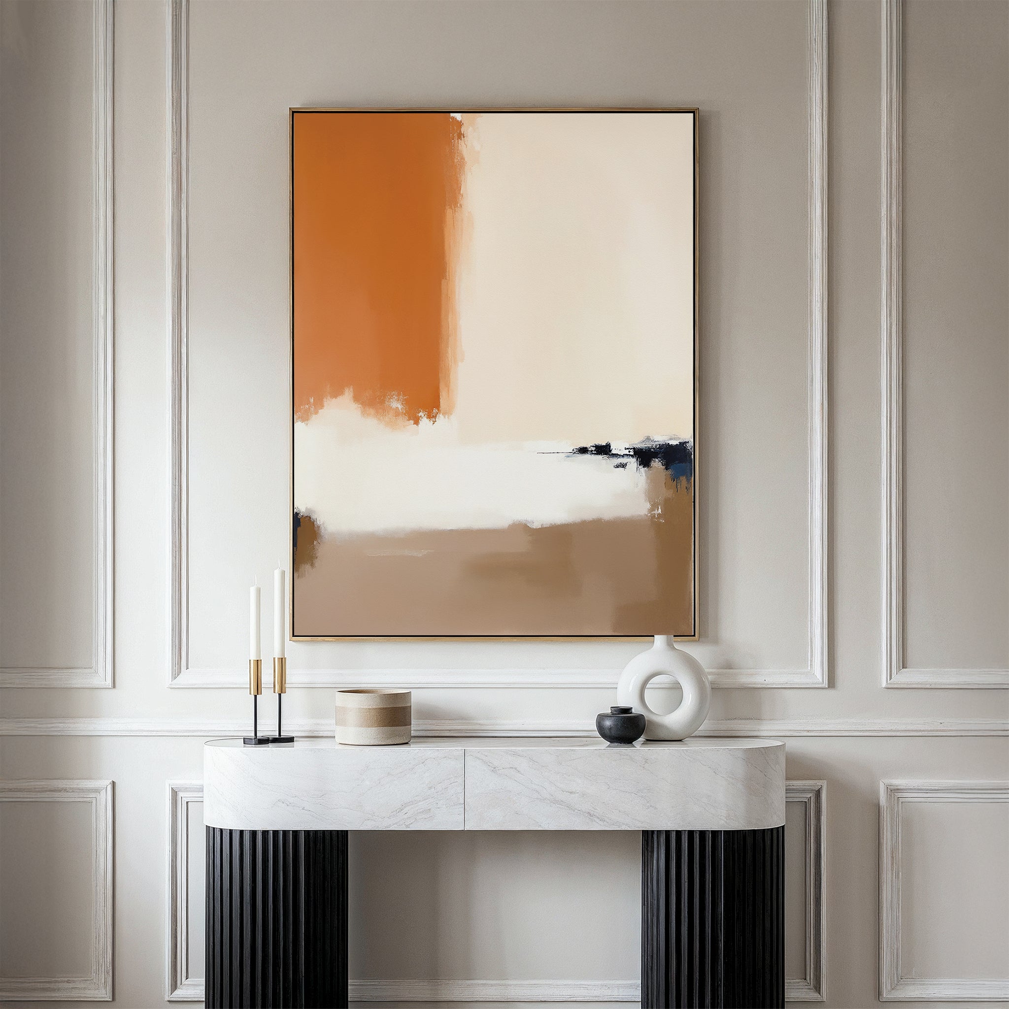 A minimalist console table with a white marble top and black legs stands against a light paneled wall, adorned with candles and decor. Above it hangs the Terracotta Edge Canvas Art - Vertical, featuring beige, black, white, and burnt orange hues.