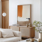 A modern, minimalist living room features a light wood sideboard, neutral ceramics, a potted plant, and a white cushioned sofa. Soft beige and tan decor is accented by the Terracotta Edge Canvas Art - Vertical and contemporary abstract prints.