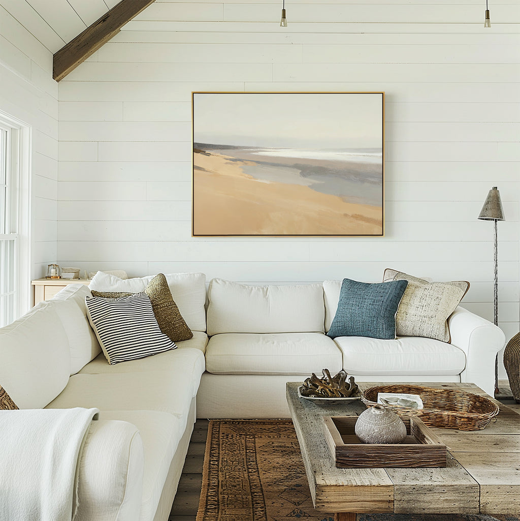 A bright, cozy living room with a white sectional sofa, textured pillows, a rustic wooden coffee table, and Tidal Meditation Canvas Art - Horizontal—a tranquil beach landscape—adorning the white shiplap walls.