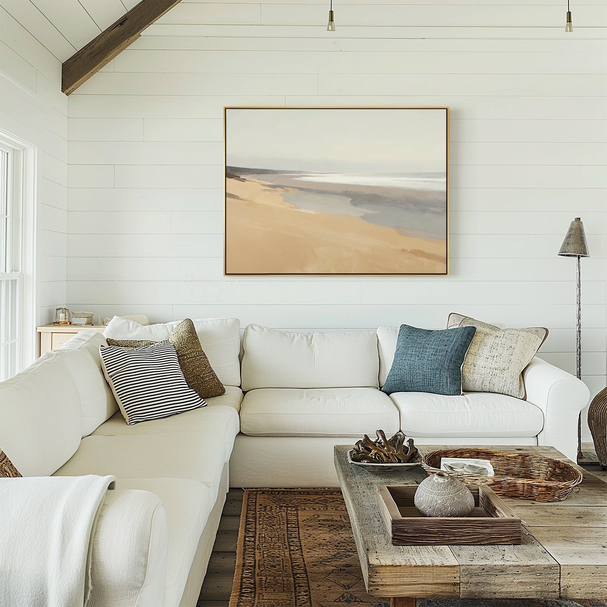 A bright, cozy living room with a white sectional sofa, textured pillows, a rustic wooden coffee table, and Tidal Meditation Canvas Art - Horizontal—a tranquil beach landscape—adorning the white shiplap walls.