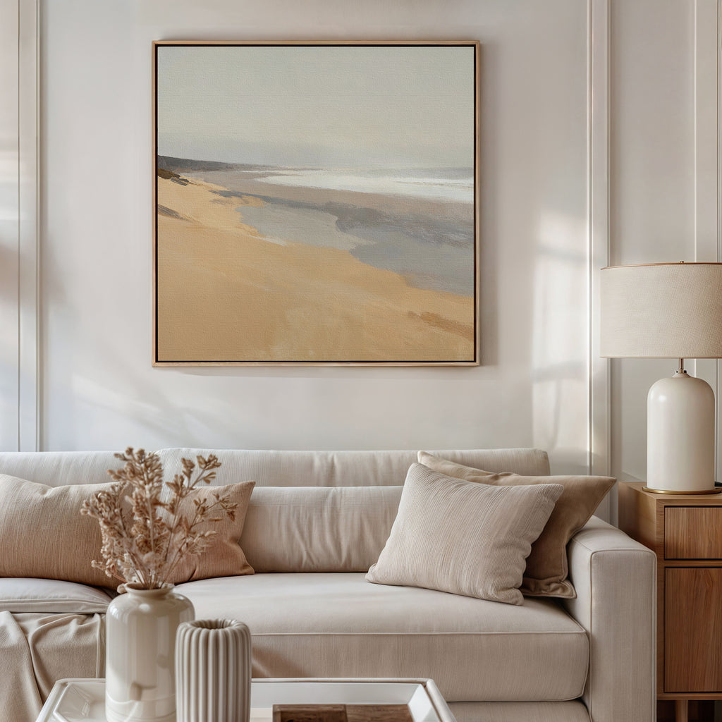 A cozy living room with a beige sofa, neutral pillows, a side table and lamp, dried flowers in a vase, and the Tidal Meditation Canvas Art - Square adding tranquil coastal vibes to the light-colored wall.