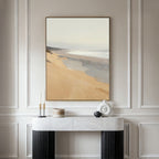 A minimalist room features a marble console table with decor beneath the “Tidal Meditation Canvas Art - Vertical,” evoking a serene beach scene on the elegant, light-paneled wall.