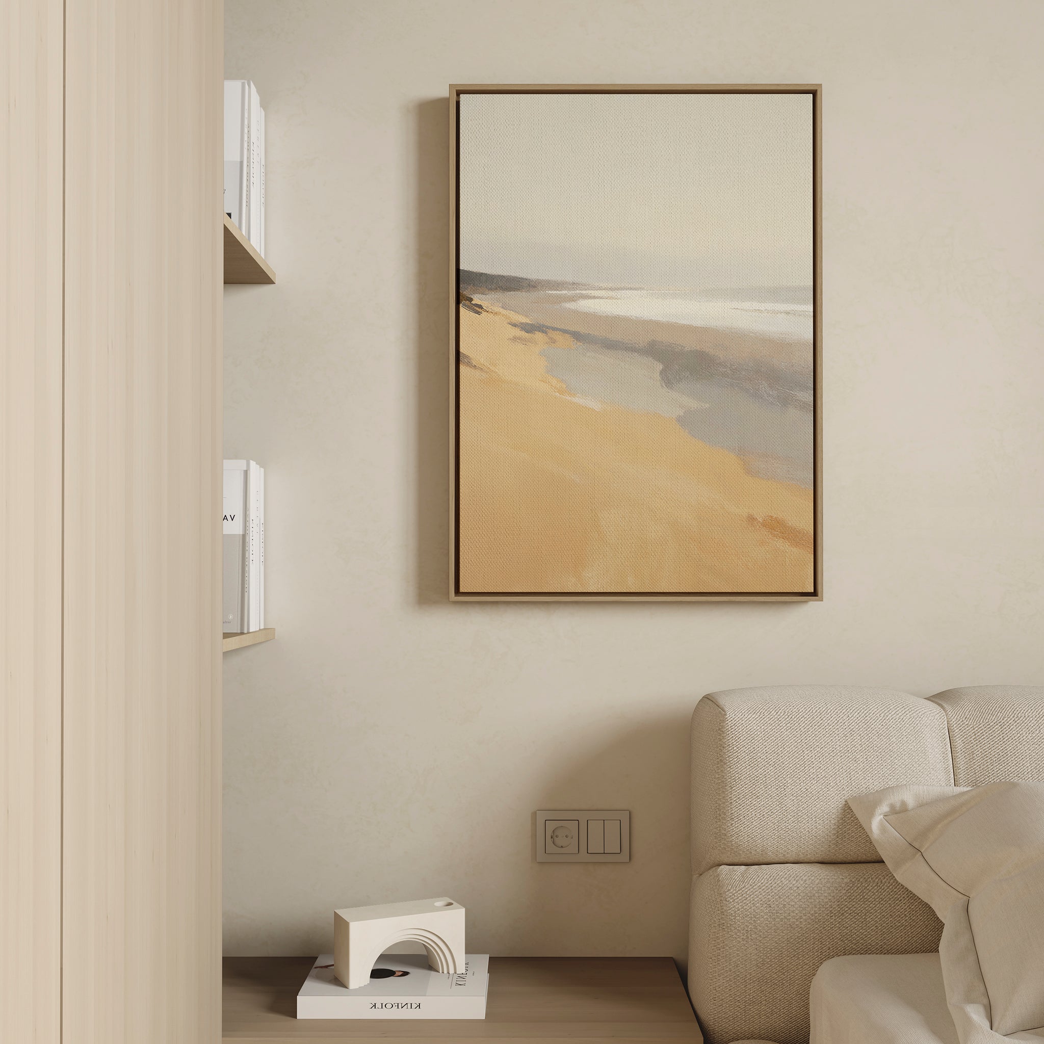 A minimal living space with a beige wall, Tidal Meditation Canvas Art - Vertical as coastal décor in a frame, a white couch, built-in bookshelves, and a small geometric lamp on a wooden floor.