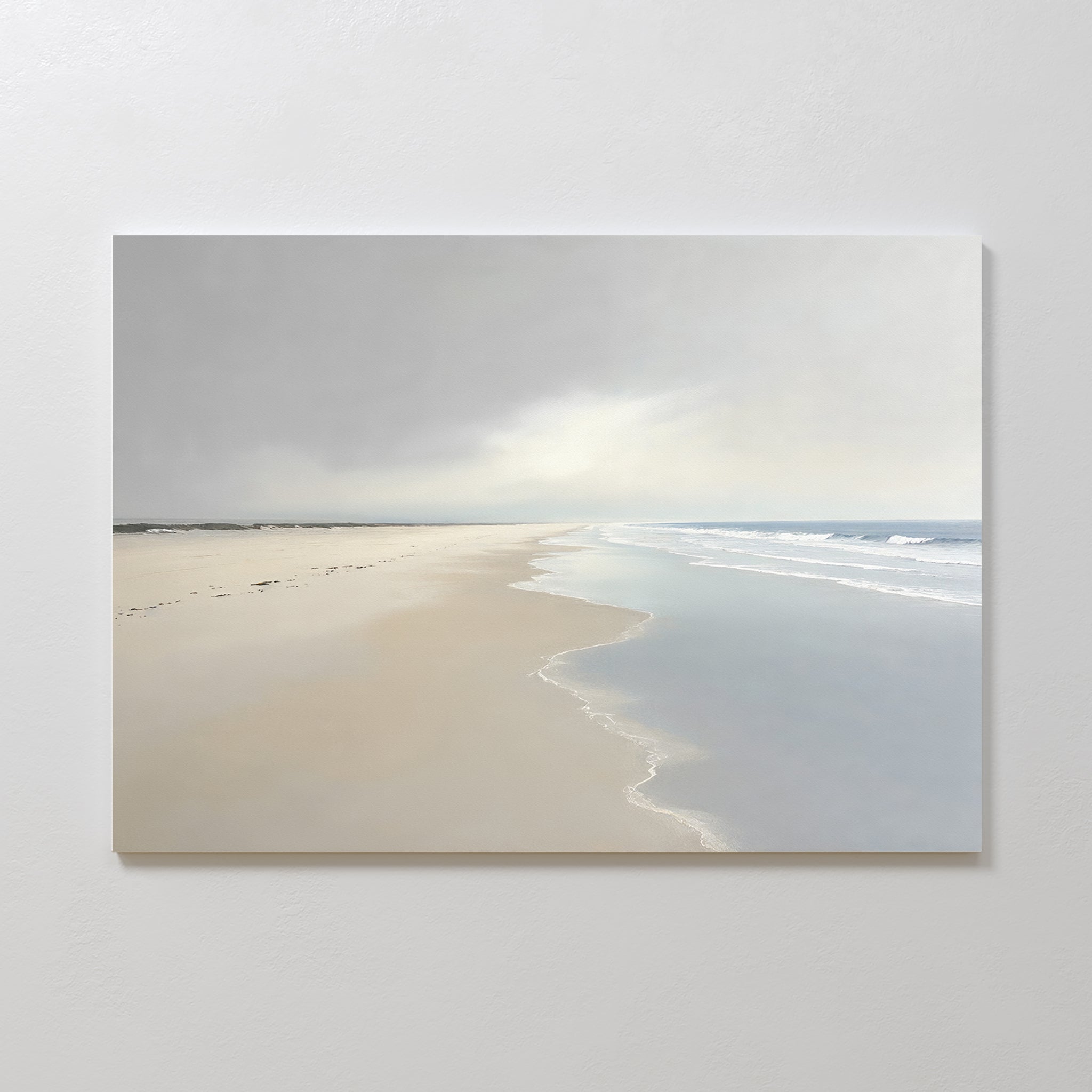 The Tidal Reflections Canvas Art - Horizontal depicts a calm, empty beach with gentle waves and footprints under a cloudy sky, making it perfect as calming wall decor for your white wall.