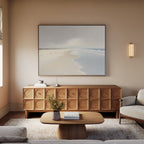 A minimal living room features a beige sofa, wooden coffee table, textured sideboard, and the Tidal Reflections Canvas Art - Horizontal above. A small plant and books add charm, while soft natural light enhances this calming wall decor.