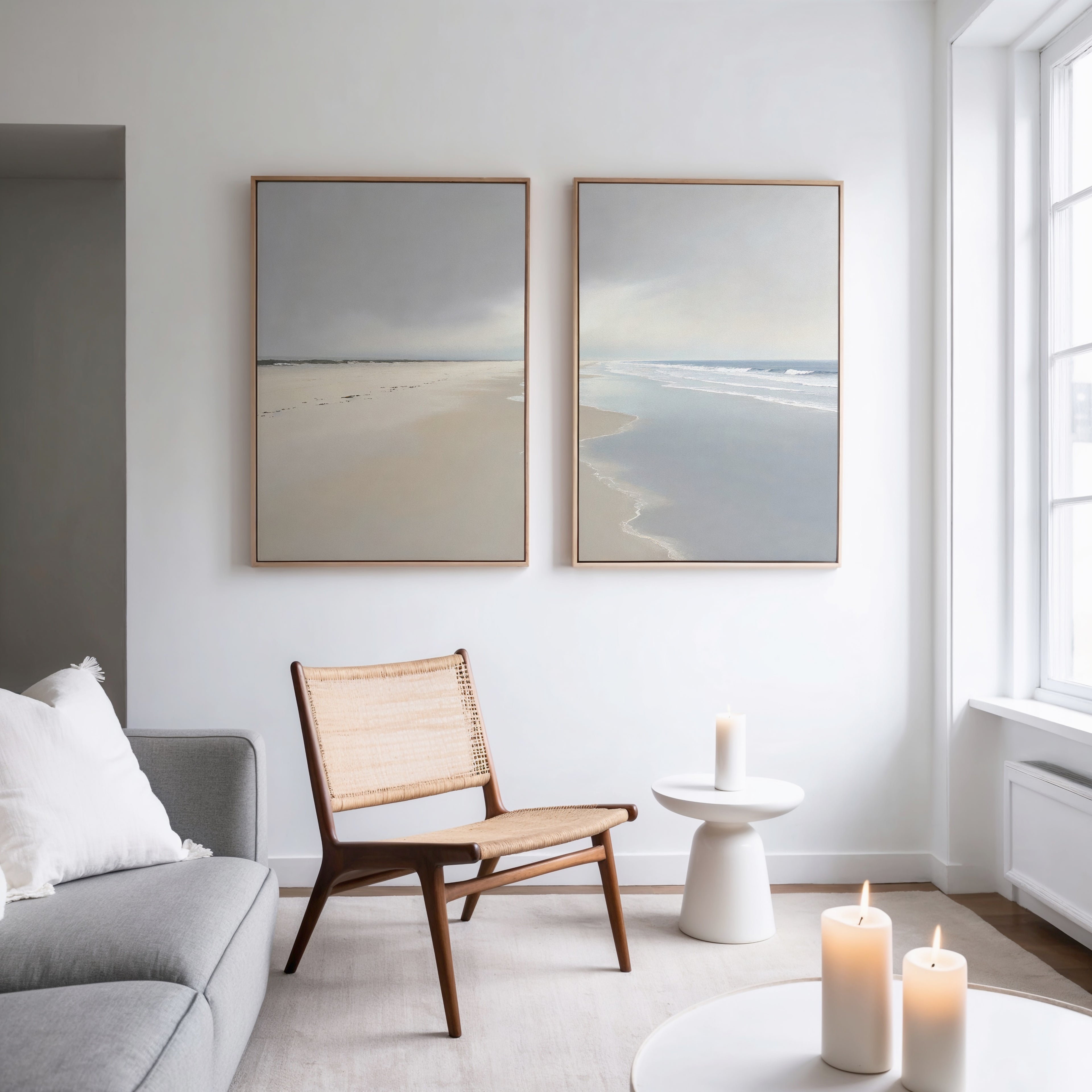 A modern living room with a light gray sofa, wooden chair, small white side table with a lit candle, and Tidal Reflections - Set of 2 ocean art prints on the wall. Sunlight pours in through large windows.