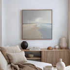 A serene, minimalist living room with a beige sofa, neutral cushions, wooden sideboard, decorative vases, and calming wall decor—a large Tidal Reflections Canvas Art - Square print of a calm beach hanging on a white wall.