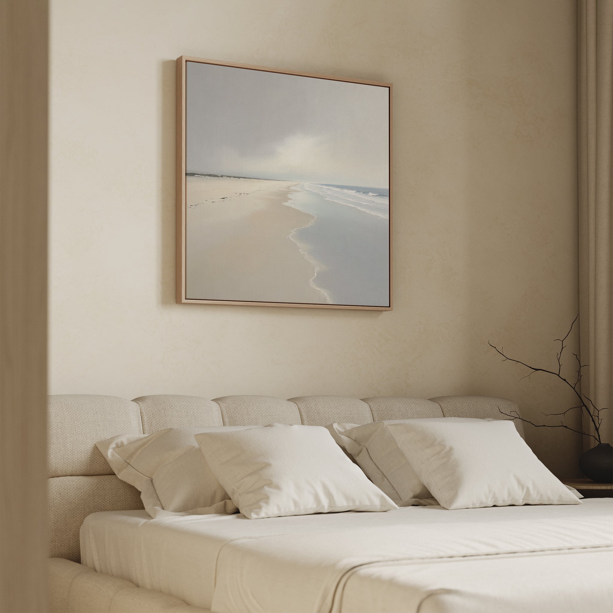 A minimalist bedroom with a beige upholstered bed, white pillows and bedding, and the Tidal Reflections Canvas Art - Square depicting a serene beach above the headboard. A bare branch in a vase on the nightstand adds to the calming decor.