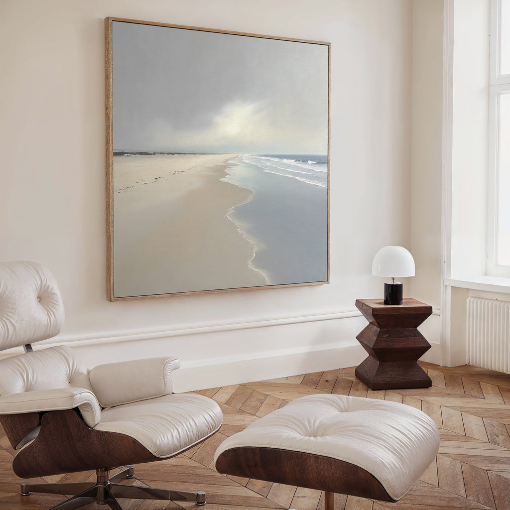 A cozy room features a white leather lounge chair and ottoman, a modern wooden side table with a small white lamp, and the Tidal Reflections Canvas Art - Square displayed on the wall. Sunlight shines in through a tall window.