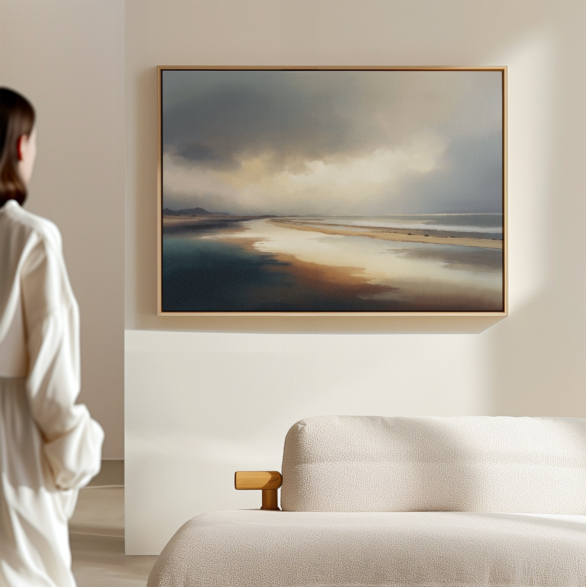 A person in a white shirt stands in a bright, minimal room, gazing at the Tidal Reverie Canvas Art - Horizontal hanging above a cream-colored couch.