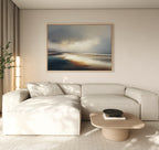 A modern living room with a light beige sectional sofa, a low wooden coffee table featuring a black bowl, a tall plant, and Tidal Reverie Canvas Art - Horizontal as coastal wall art above the sofa. Neutral tones create a calm atmosphere.