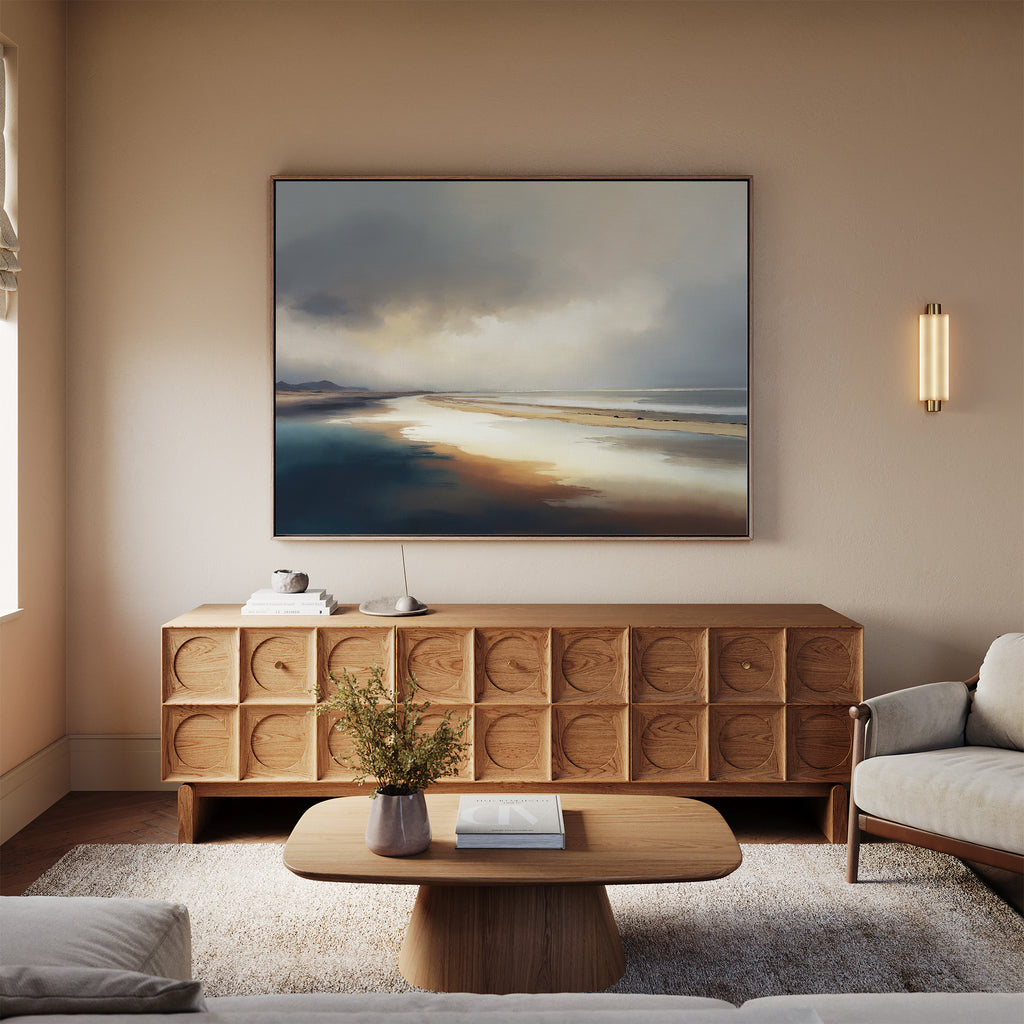 A modern living room features a light sofa, wooden coffee table with a small plant, and a sideboard with circular patterns. Above the sideboard hangs the Tidal Reverie Canvas Art - Horizontal, while a wall sconce provides light.