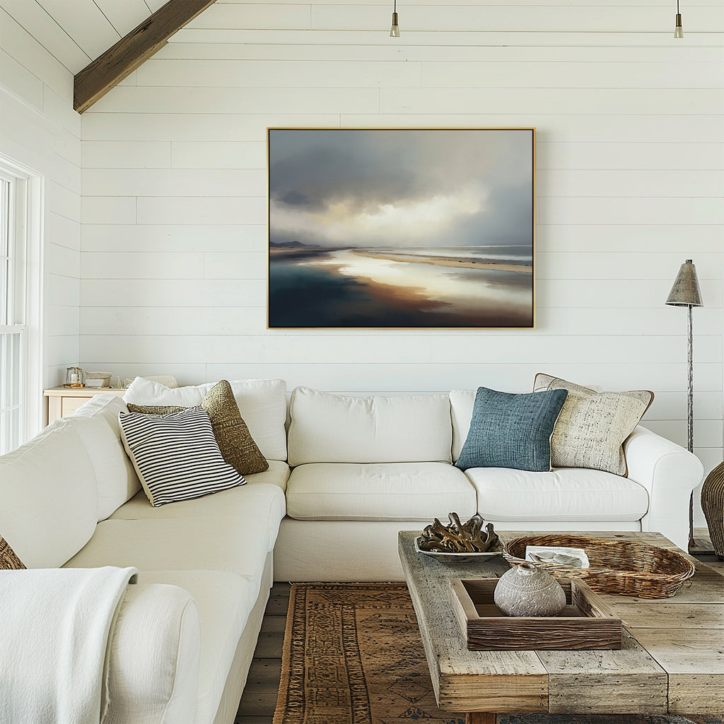 A bright, airy living room with white shiplap walls, a large white sectional sofa with assorted pillows, a rustic wooden coffee table, and the Tidal Reverie Canvas Art - Horizontal featuring a cloudy sky and water displayed above the couch.