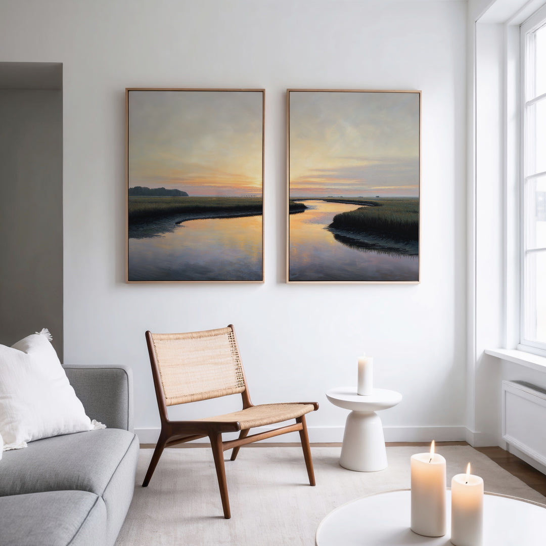 A modern living room with a wooden chair, white sofa, lit candles, and Tidal Whispers - Set of 2 large sunset-over-water canvas prints on a white wall near a tall window.