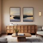 A modern living room with a wooden sideboard, coffee table, and light gray sofa. The "Tidal Whispers - Set of 2" canvas prints and a wall sconce hang above the sideboard, while a small plant and books are on the table.