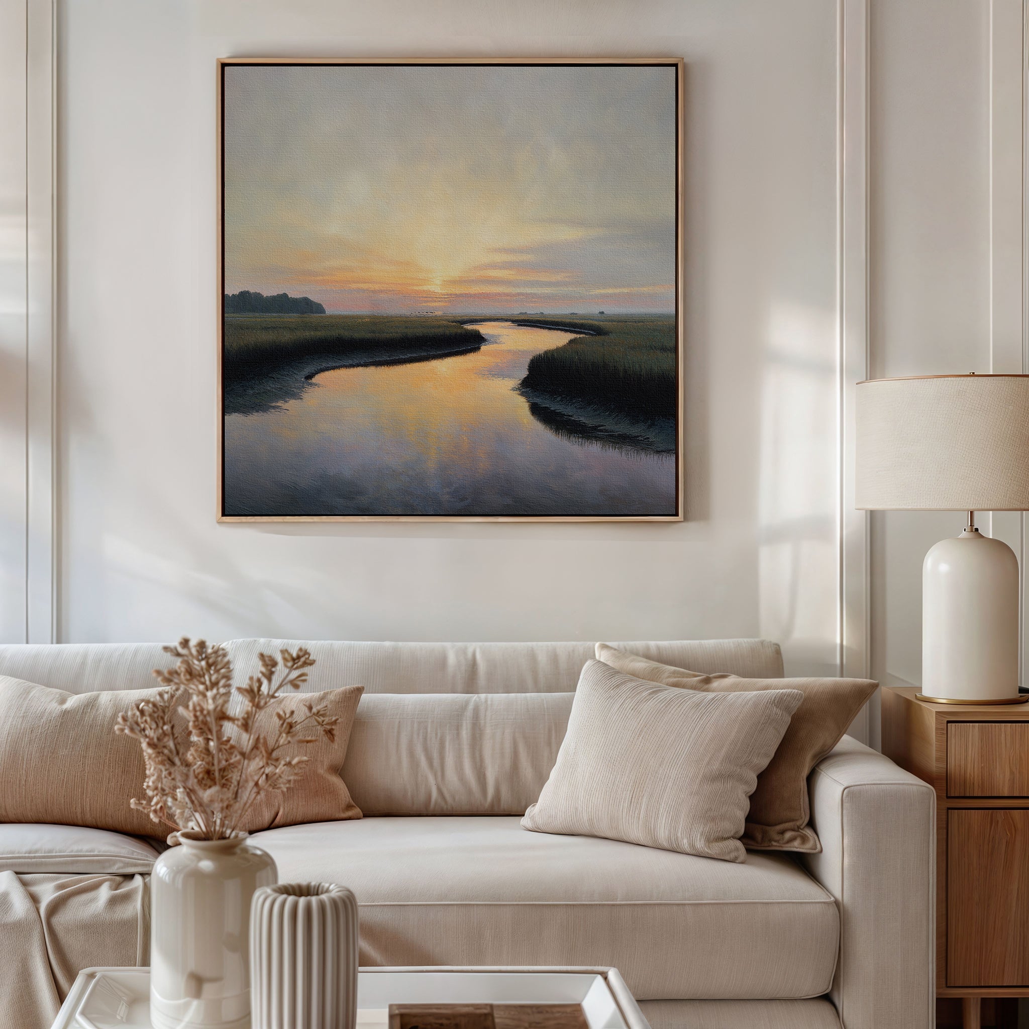 A modern living room with a beige sofa, neutral cushions, a side table with a lamp, dried flowers in vases, and the Tidal Whispers Canvas Art - Square depicting a serene river at sunset hanging above the couch.