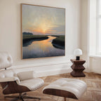 A cozy, modern living room features a white lounge chair and ottoman, a geometric wooden side table with a small white lamp, and the Tidal Whispers Canvas Art - Square as sunset-inspired wall decor above the serene space.