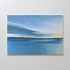 The Tranquil Reflections Canvas Art - Horizontal shows a serene blue lake beneath a blue sky with dark clouds and yellow light at the horizon, elegantly mounted on a plain white wall.
