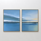 The "Tranquil Reflections - Set of 2" features framed canvas prints of a serene blue lake with water, sky, hills, and clouds; the right print adds yellow sunlight. This calming wall art pair hangs side by side on a white wall.