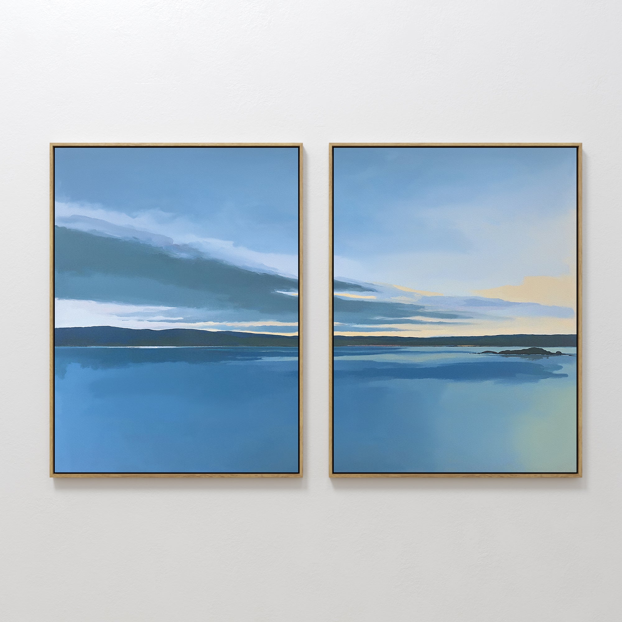 The "Tranquil Reflections - Set of 2" features framed canvas prints of a serene blue lake with water, sky, hills, and clouds; the right print adds yellow sunlight. This calming wall art pair hangs side by side on a white wall.
