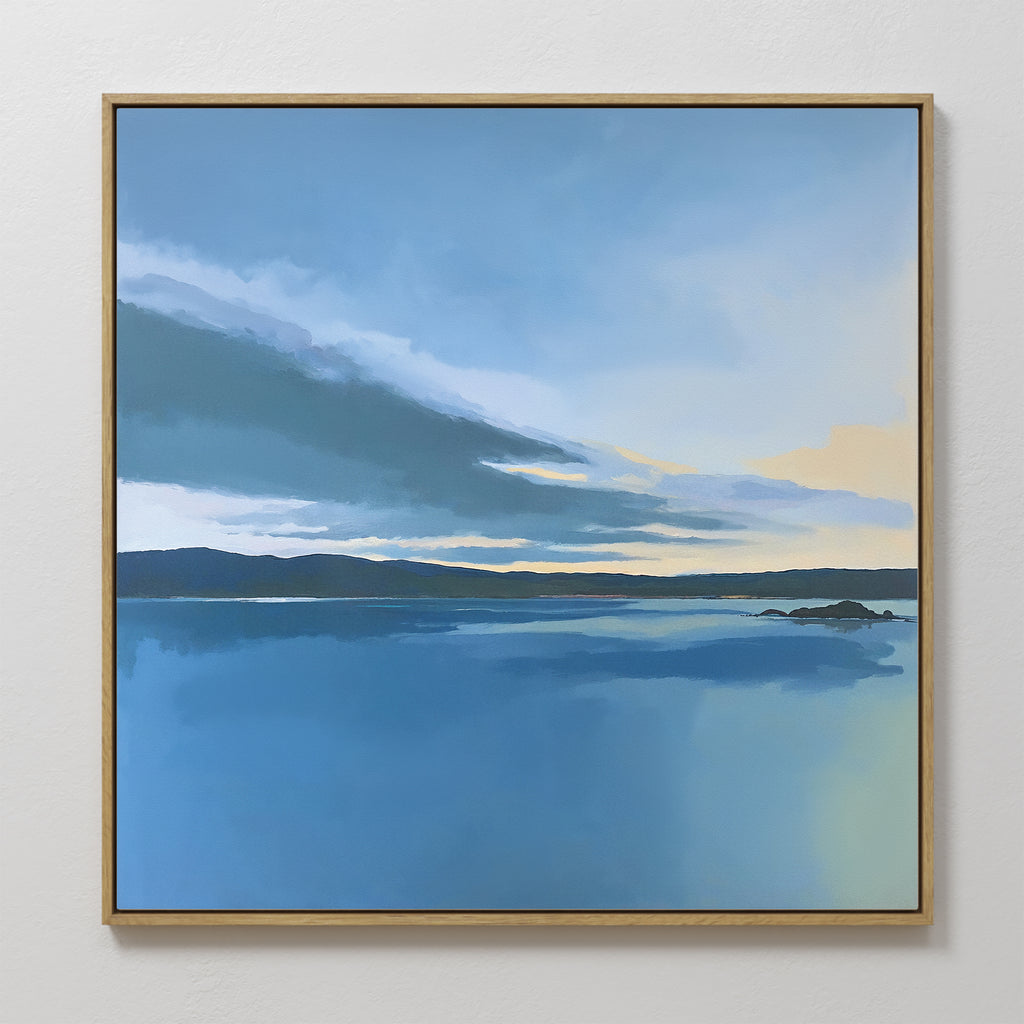 The Tranquil Reflections Canvas Art - Square features a calm blue lake with a distant shoreline beneath a blue, gray, and yellow sky, evoking sunrise or sunset. Serene and softly rendered, it’s ideal for tranquil bedroom decor.