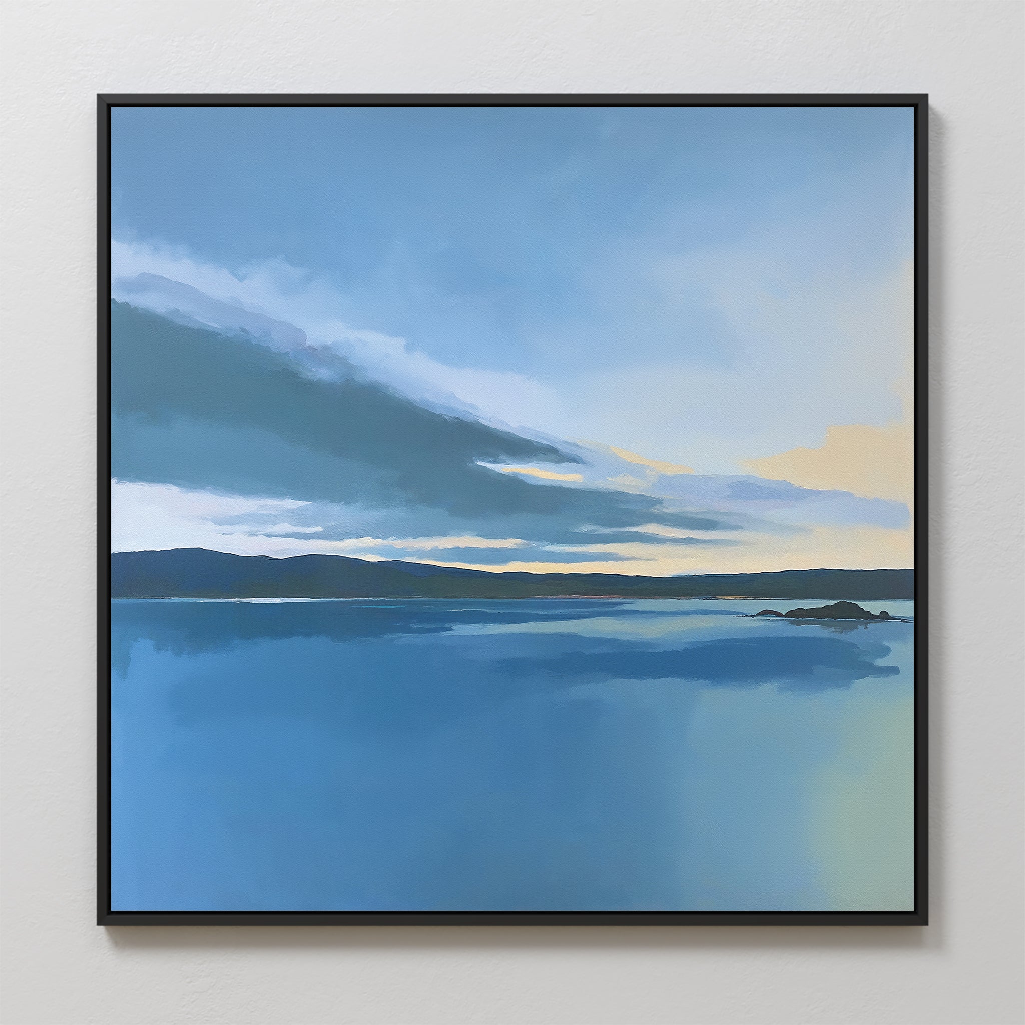 The Tranquil Reflections Canvas Art - Square showcases a calm blue lake with distant hills at sunrise or sunset, featuring soft yellow and blue tones—ideal serene wall art for tranquil bedroom decor on a light-colored wall.