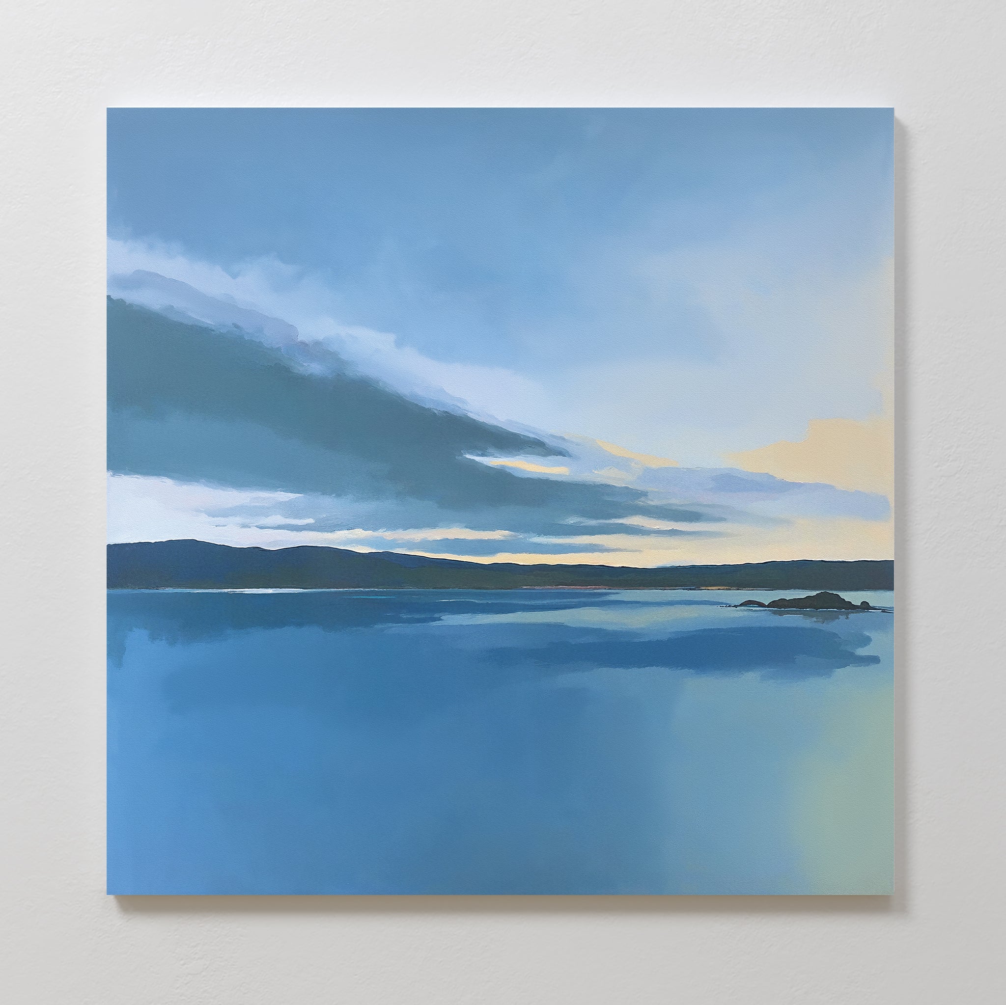 The "Tranquil Reflections Canvas Art - Square" features a calm sea, distant hills, and a cloudy blue sky with yellow sunrise or sunset accents—ideal serene wall art to enhance tranquil bedroom decor.
