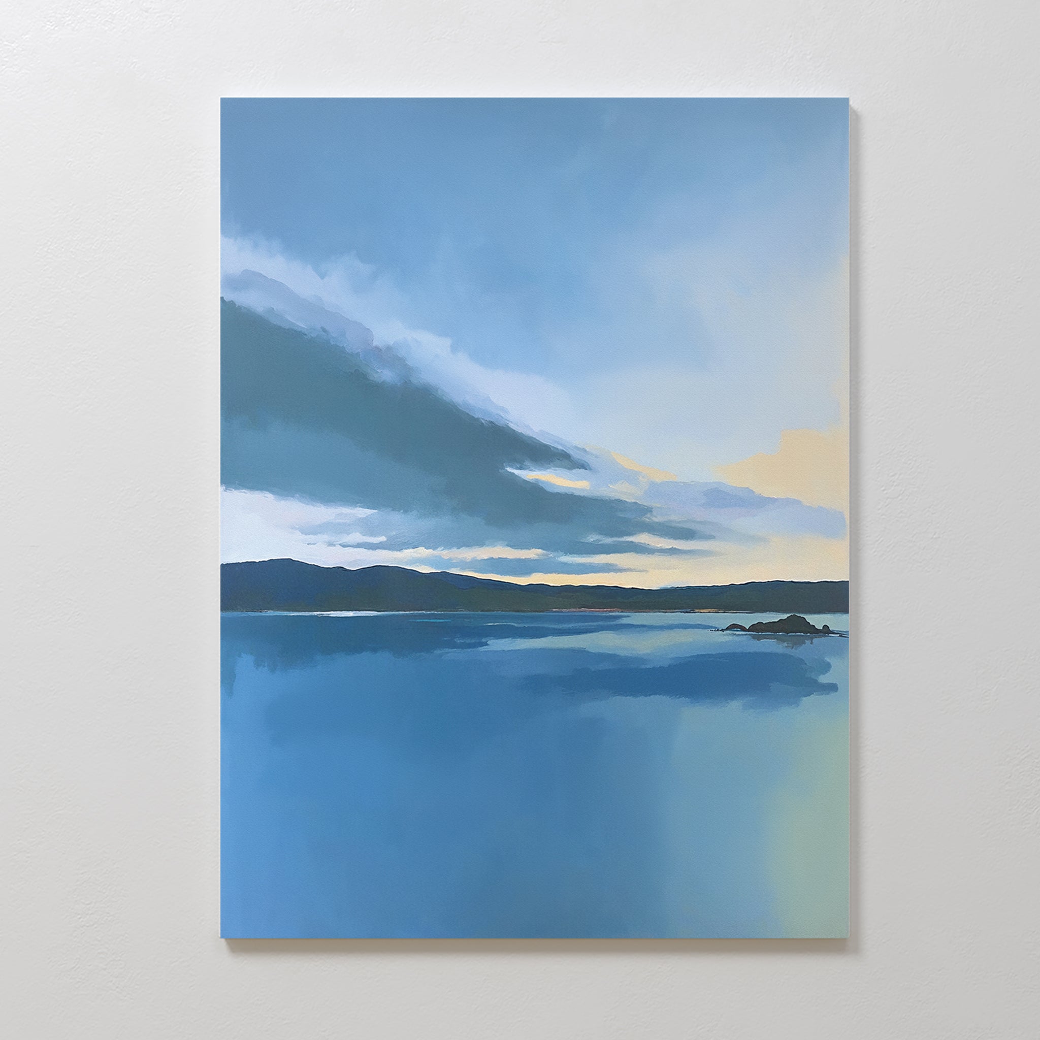 The Tranquil Reflections Canvas Art - Vertical features a serene blue lake mirroring the sky with distant hills and clouds, displayed on a plain white wall.