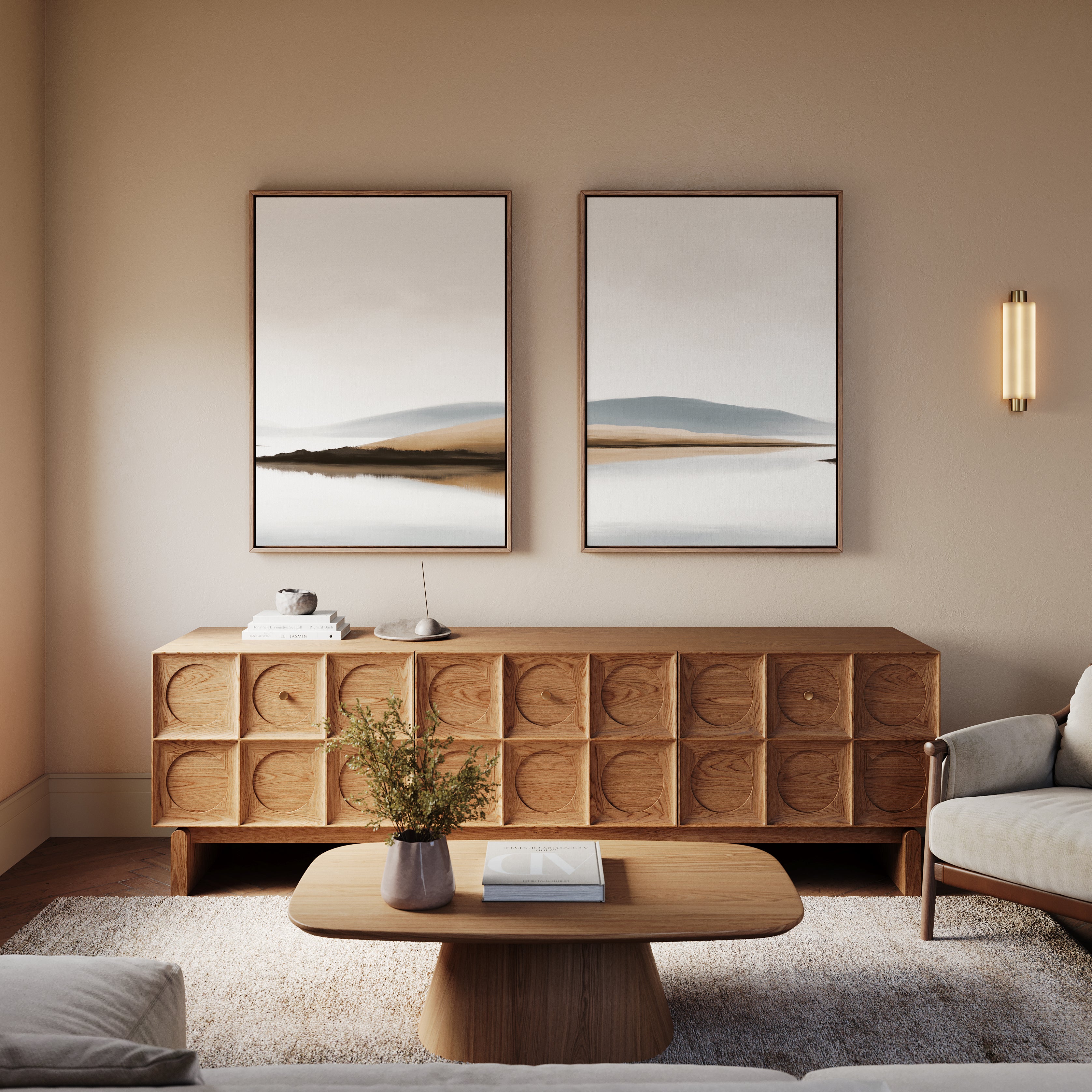 A minimalist living room featuring light walls, a wooden sideboard with carved cube patterns, the Tranquil Waters - Set of 2 wall art, a round coffee table, gray sofa, small vase with greenery, and a modern wall sconce.