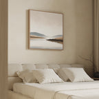 A modern bedroom features a beige upholstered bed with white bedding, and the Tranquil Waters Canvas Art - Square above the headboard. A dry branch in a vase adds a natural touch to the serene lakeside setting.
