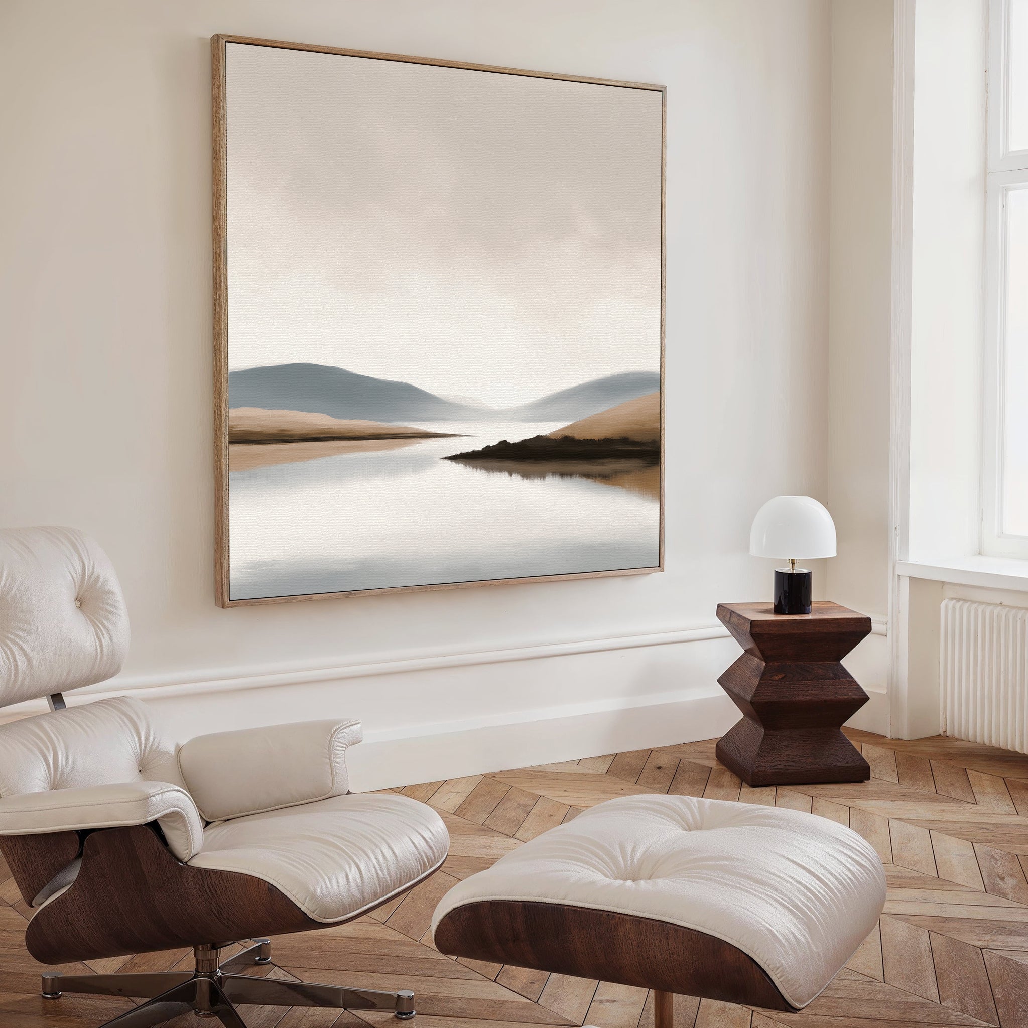 A modern living room with a white leather lounge chair and ottoman, a geometric dark wood side table with a small white lamp, and the Tranquil Waters Canvas Art - Square as the focal point of the decor.