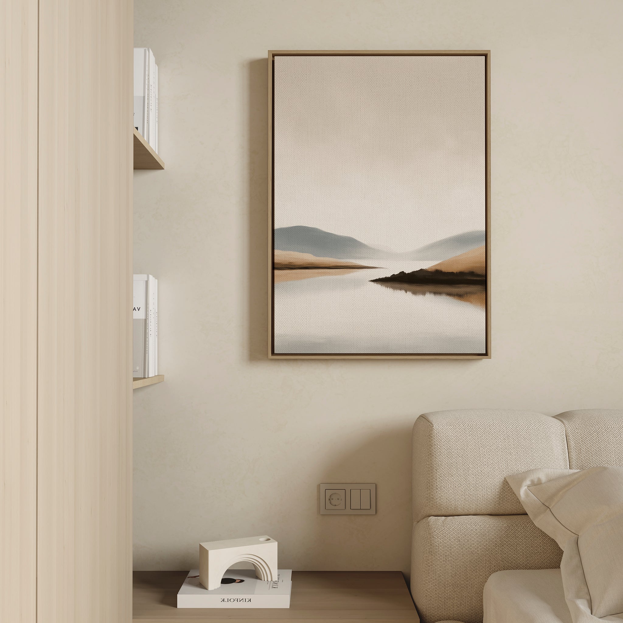 Minimalist living room with a beige sofa, built-in shelves, and the Tranquil Waters Canvas Art - Vertical featuring mountains and a lake on a light wall. A small white geometric decor piece is displayed on the lower shelf.