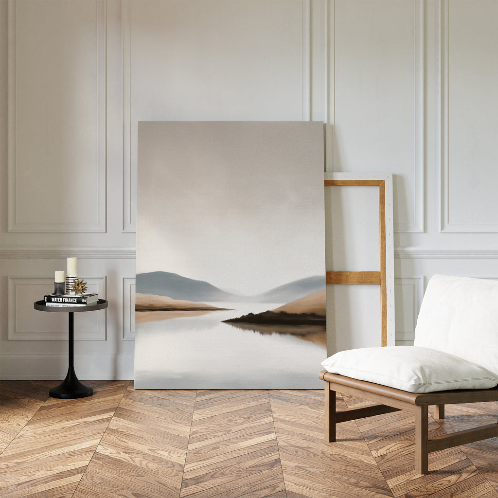 A minimalist living room showcases the Tranquil Waters Canvas Art - Vertical, featuring a serene mountain and lake scene, propped against a white paneled wall beside a white cushioned chair and black side table on herringbone wood flooring.