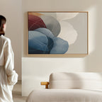 A person stands in a minimalist room with a light-colored sofa and "Translucent Petals Canvas Art - Horizontal," an abstract painting with blue, white, and brown shapes, hanging on the wall.