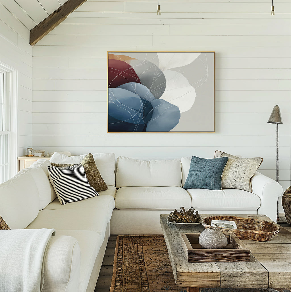 A cozy living room with a white sectional sofa, pillows, and a rustic wood coffee table. Above the sofa on the white shiplap wall hangs the Translucent Petals Canvas Art - Horizontal showcasing blue, white, and burgundy shapes.