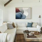 A cozy living room with a white sectional sofa, pillows, and a rustic wood coffee table. Above the sofa on the white shiplap wall hangs the Translucent Petals Canvas Art - Horizontal showcasing blue, white, and burgundy shapes.