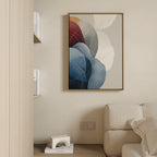 A modern living room with a beige sofa, light wood shelves holding books, and the Translucent Petals Canvas Art - Vertical featuring blue, red, and white shapes. A small decorative object sits on the shelf below.