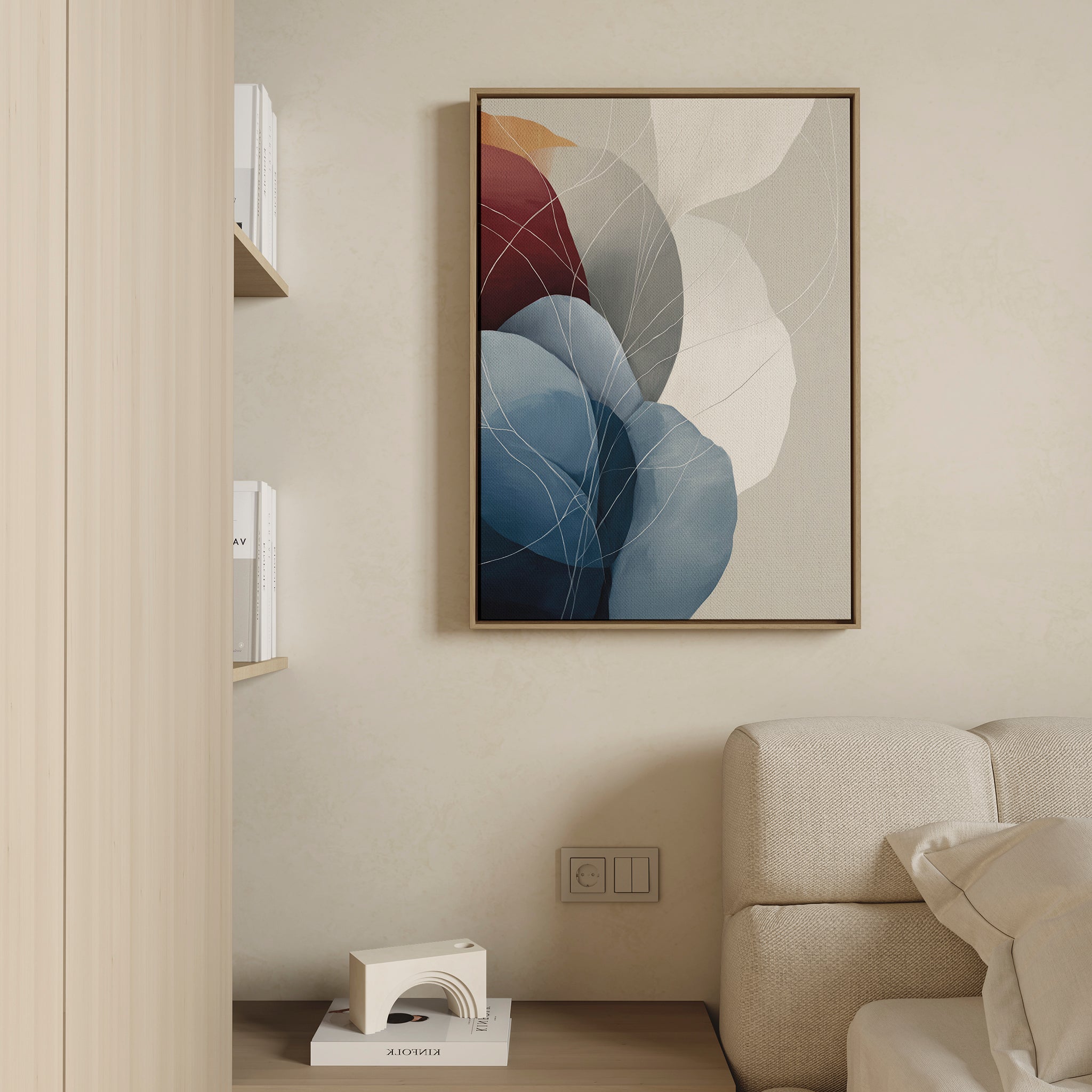 A modern living room with a beige sofa, light wood shelves holding books, and the Translucent Petals Canvas Art - Vertical featuring blue, red, and white shapes. A small decorative object sits on the shelf below.