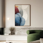 A modern living room with a green curved sofa, marble accents, a small vase with dried branches, and the Translucent Petals Canvas Art - Vertical featuring blue, red, and neutral hues on a light-colored wall.