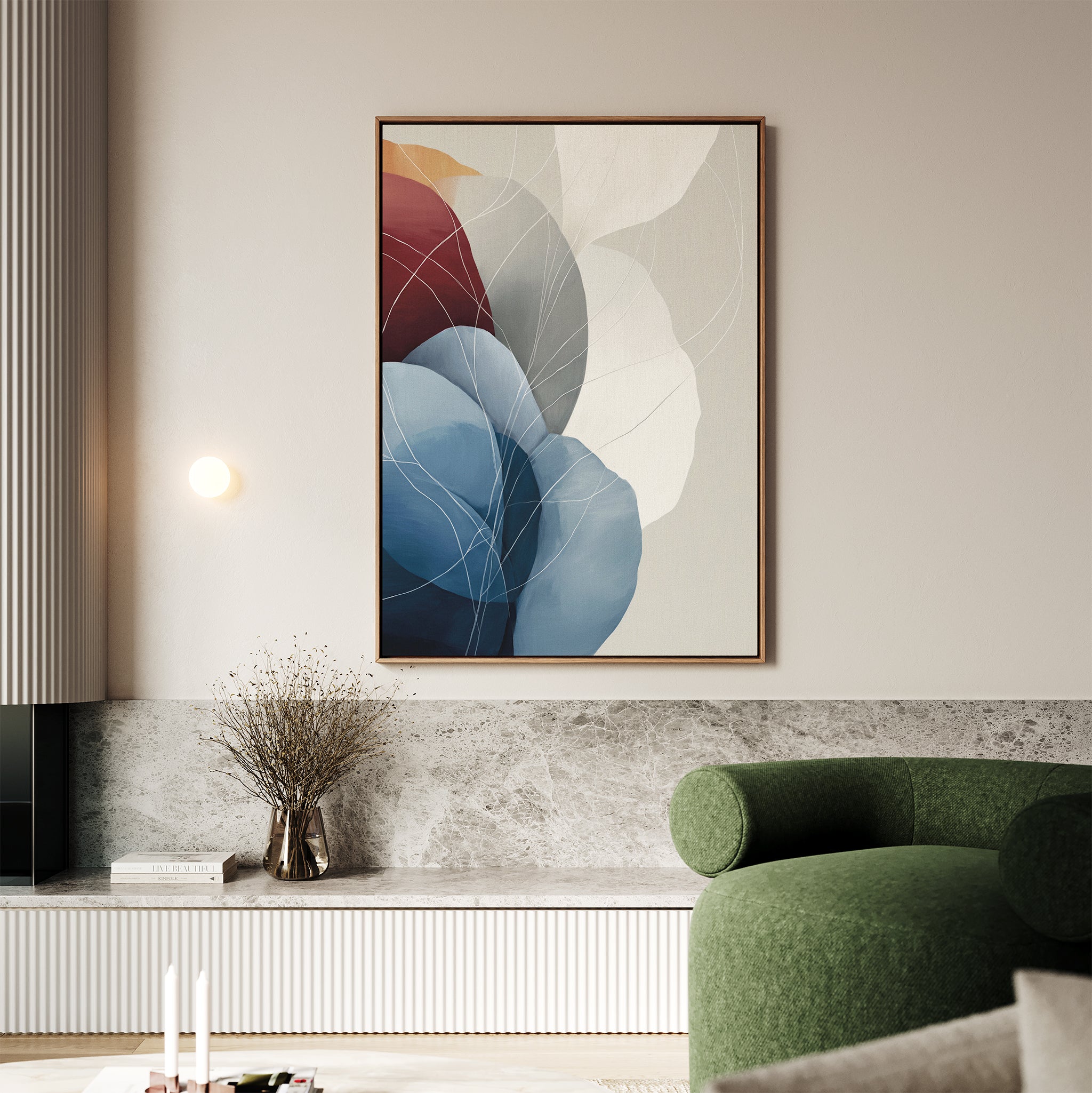 A modern living room with a green curved sofa, marble accents, a small vase with dried branches, and the Translucent Petals Canvas Art - Vertical featuring blue, red, and neutral hues on a light-colored wall.