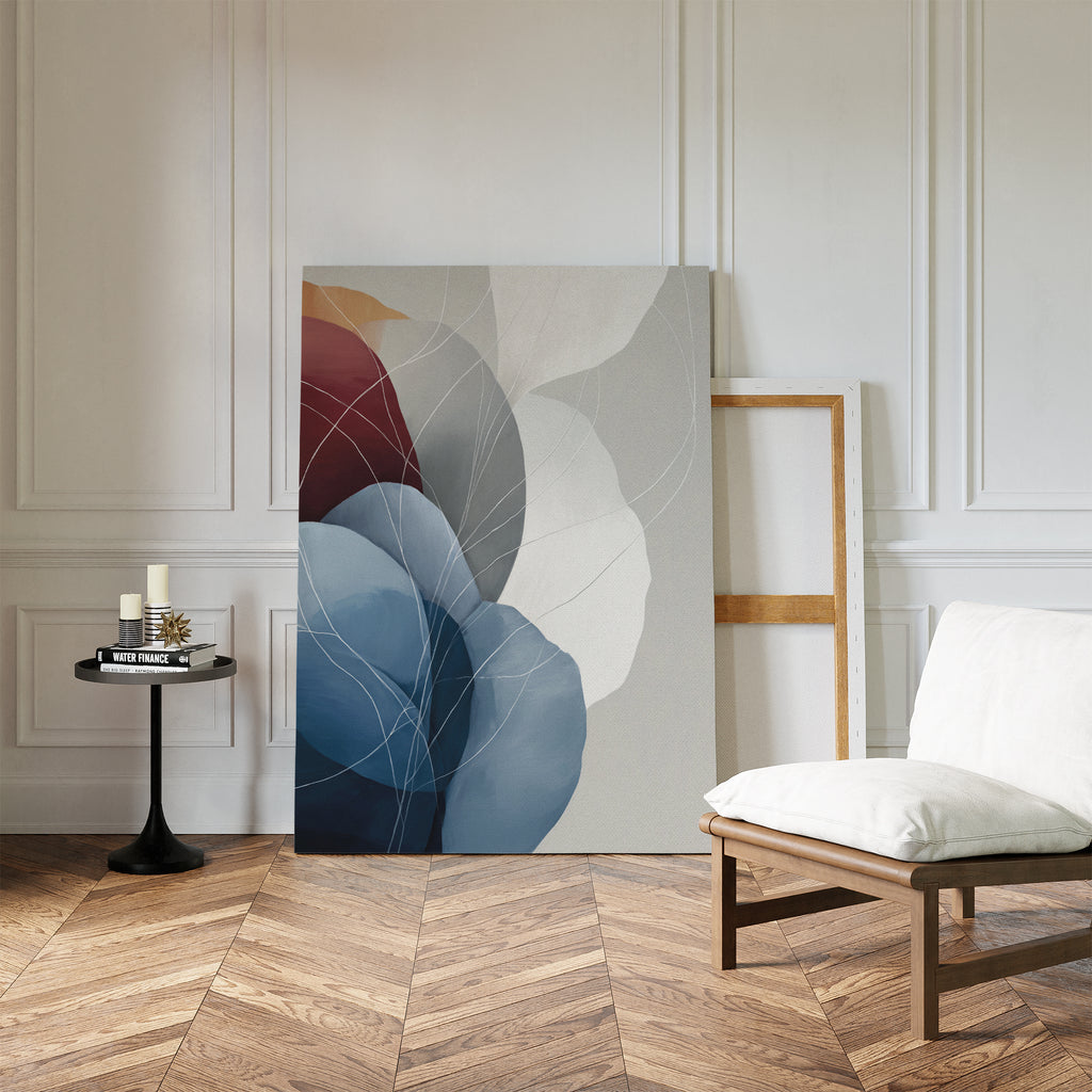 A modern, minimalist room with herringbone wood floors and white paneled walls features the Translucent Petals Canvas Art - Vertical leaning against the wall. A low cushioned chair and a black side table with books and candles complete the look.