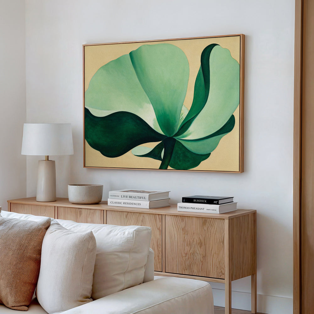 A modern living room features a wooden sideboard, stacked books, a lamp, and a beige couch. Above the sideboard on the white wall hangs the Tropical Serenity Canvas Art - Horizontal, showcasing an abstract green floral design.