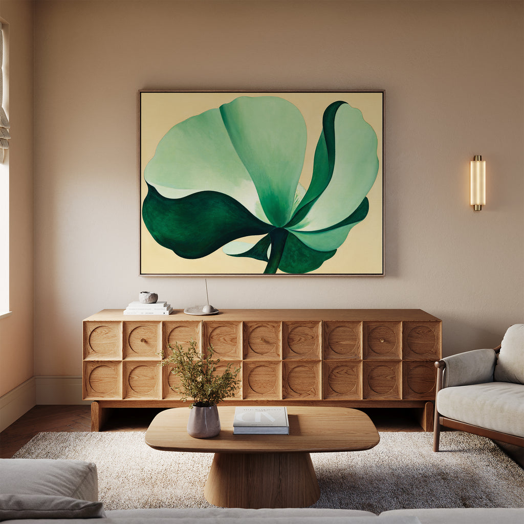 A modern living room with light walls, the Tropical Serenity Canvas Art - Horizontal above a wooden sideboard, a round wooden coffee table, a white sofa, fresh flowers in a vase, and a wall sconce creates an inviting and relaxed atmosphere.