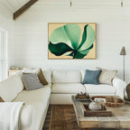 A cozy living room with a white sectional sofa, patterned pillows, a rustic wooden coffee table, and the Tropical Serenity Canvas Art - Horizontal showcasing abstract green and blue botanicals on the white shiplap wall.
