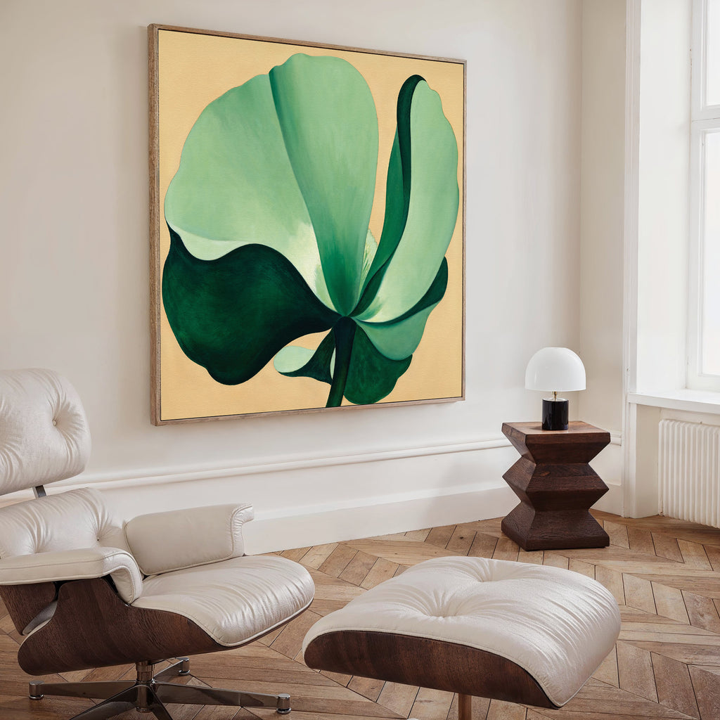 A modern living room with a white lounge chair and ottoman, dark wood side table and small white lamp, featuring the Tropical Serenity Canvas Art - Square. Light herringbone wood floor and a tall window complete the look.