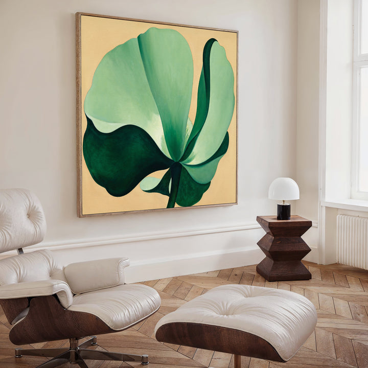 A modern living room with a white lounge chair and ottoman, dark wood side table and small white lamp, featuring the Tropical Serenity Canvas Art - Square. Light herringbone wood floor and a tall window complete the look.